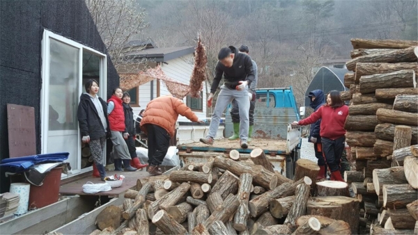 (사진3)학생들이 장작을 자른 후에 집 옆에 나르고 쌓아 올리고 있다