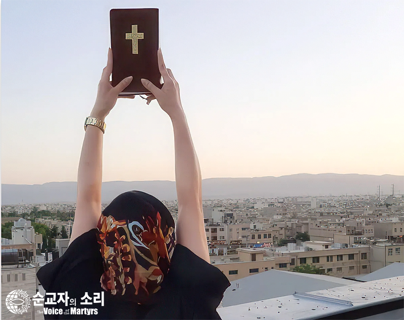 이란의 한 기독교인이 두 손 높이 성경을 들고, 도시 정경을 내려다 보고 있다.     